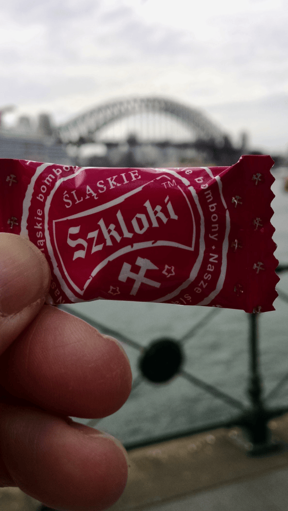 Holding a Śląskie Szkloki wrapped sweet, in blurry background is Sydney Harbour bridge